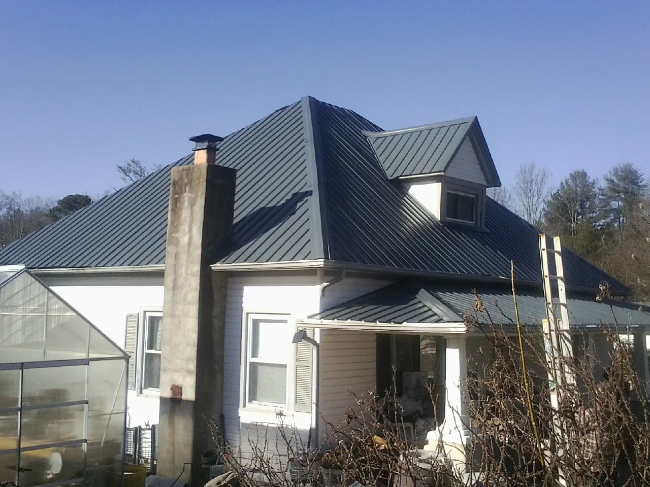 Dark blue standing seam metal roof on a white farmhouse with dormer — Slate & Tile Roof Repair by Roofing Brothers in Cooksville