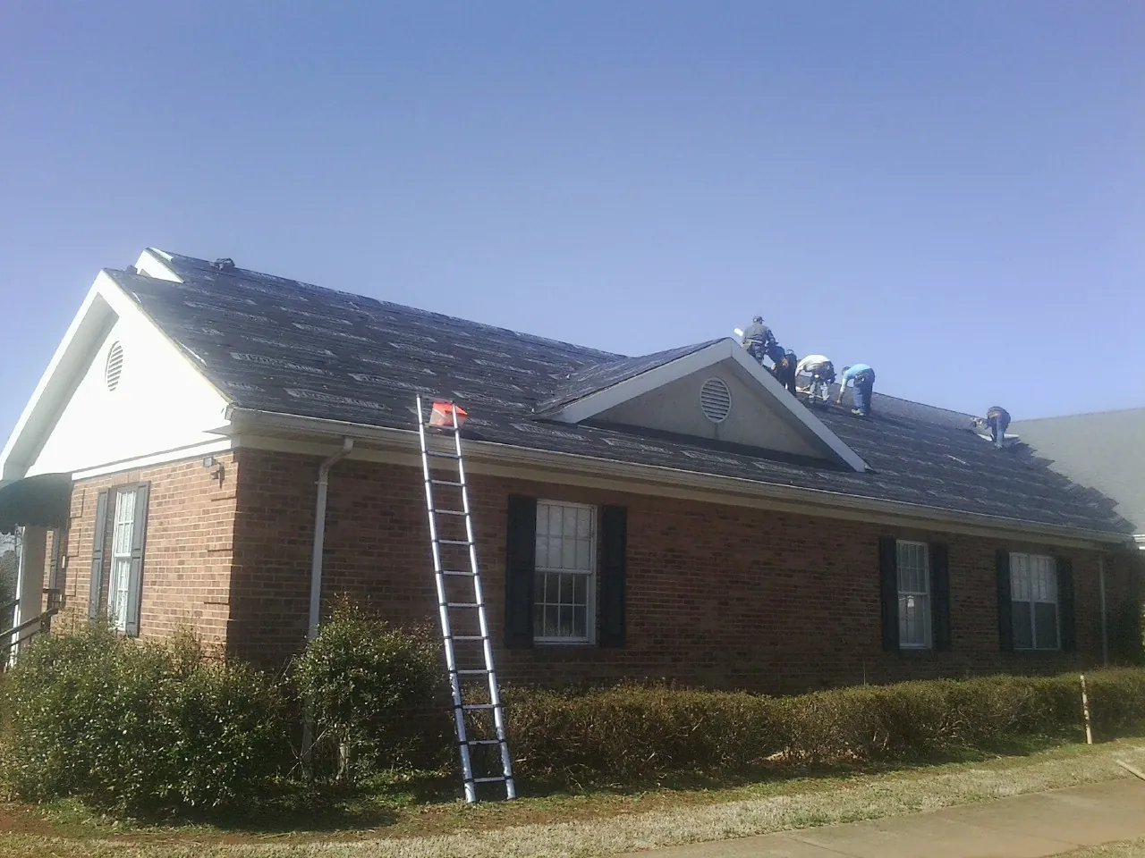 Crew tearing shingles off a brick ranch roof with a ladder set — Metal Roof Repair work by our crew in Cooksville
