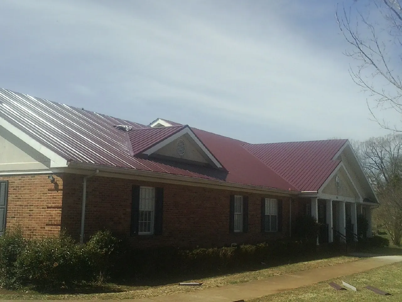 Red metal roof with gabled entries on a long brick building, from a Hail Damage Roof Repair job in Cooksville
