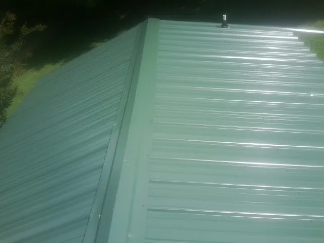 New green metal panels meeting at the ridge of a roof — Flat Roof Repair work by our crew in Cooksville