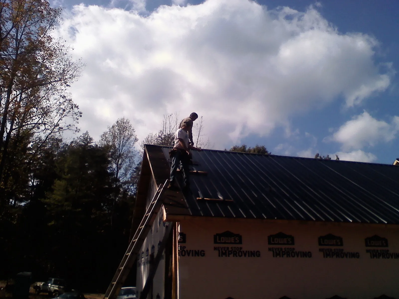 Roofer fastening dark metal panels high against a cloudy sky, from a Roof Inspection job in Cooksville