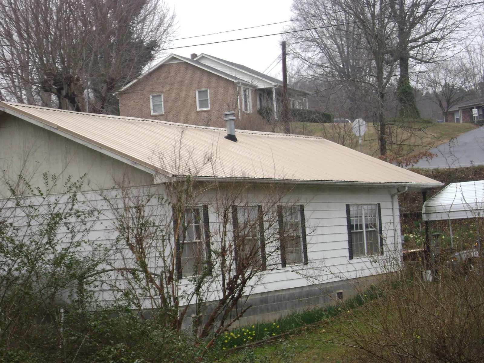 Tan metal roof on a white sided house set into a hillside — Commercial Roofing by Roofing Brothers in Cooksville